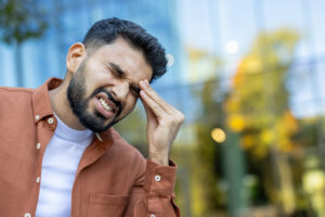 A man experiencing a headache, clutching his head in visible discomfort outdoors.